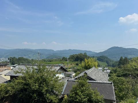 A stack of bedding sits on a brown mat in a room with tatami mats and a person standing nearby.