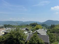 A stack of bedding sits on a brown mat in a room with tatami mats and a person standing nearby.