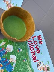 An overhead shot of a bowl of green matcha beside a "We Love Ujicha!" book on a gray surface.