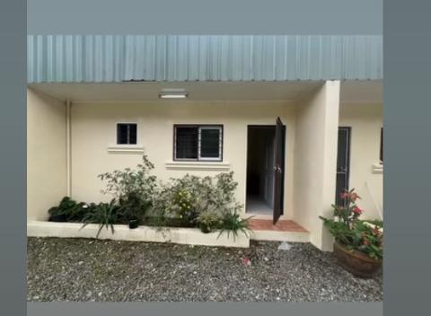 2026 - Mt. Hagen Festival Package Papua New Guinea A cream-colored building with a corrugated metal roof and a small yard with gravel and plants.