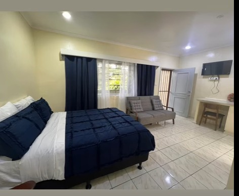 2026 - Mt. Hagen Festival Package Papua New Guinea A tidy hotel room with a large bed, a sofa, a desk, and a TV is displayed.