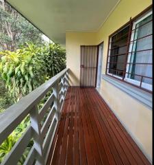 2026 - Mt. Hagen Festival Package Papua New Guinea A wooden balcony overlooks lush greenery with a yellow wall and a barred window.