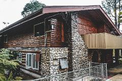 2026 - Mt. Hagen Festival Package Papua New Guinea A rustic log cabin with a stone chimney and balcony stands amidst lush greenery.