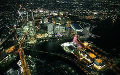 A high-angle night view of a brightly lit city, showcasing its skyscrapers, waterfront area, and a prominent Ferris wheel.
