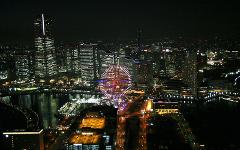 An aerial view of a brightly lit cityscape at night, featuring a large Ferris wheel and numerous skyscrapers along the waterfront.