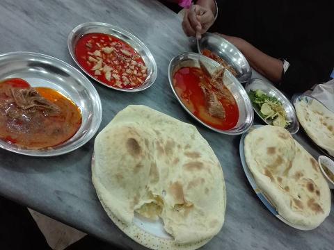 A spread of South Asian cuisine on a table, featuring naan bread, curries in metal dishes, and a side of salad.