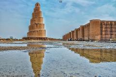 A spiral tower and long brick wall are reflected in puddles on the ground under a cloudy sky.