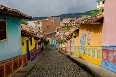 Gran Tour incluyendo Bogotá, Medellín, Nuquí y Valle del Cocora - 11 Días A street in Guatapé, Colombia, with colorful buildings lining a cobblestone road leading towards distant mountains under a cloudy sky.