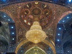 A breathtaking view of a massive chandelier hanging from an intricately decorated, mosaic-covered dome with stained glass windows.