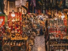 A vibrant Middle Eastern bazaar overflows with handcrafted goods, jewelry, and ornaments, illuminated by hanging lights. A man browses in the background.