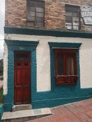 A colorful building with a teal and white facade, featuring a wooden door and window, sits beneath a brick upper level.
