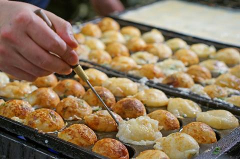 A person uses a skewer to prepare takoyaki, a Japanese snack of battered octopus balls, in a specialized pan with round molds.