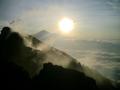 A breathtaking view from a mountain peak, shrouded in mist, with the sun shining brightly above a sea of clouds.