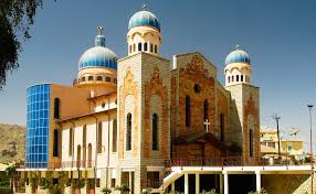 Here's a description of the image within the character limit:A colorful church with blue domes and a mix of stone and modern glass architecture stands against a clear blue sky.