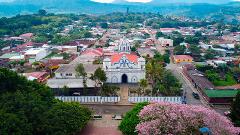 An aerial view showcases a town with a prominent church featuring a red roof and blue accents, surrounded by buildings and lush greenery.
