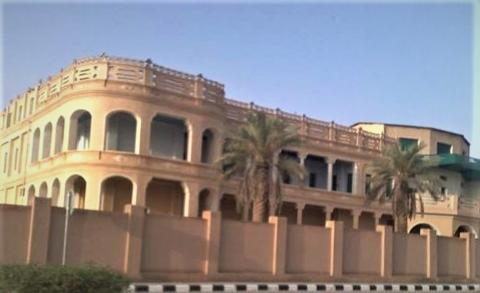 A building with arches and two palm trees in front of a wall.
