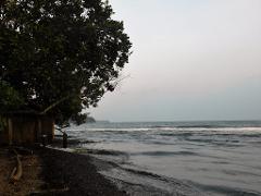 A serene view of the beach at Alotau, with a small wooden shack nestled among trees on the shoreline, creating a tranquil coastal scene.