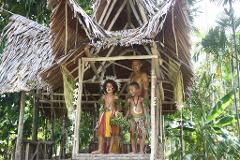 Alotau – Milne Bay Day Tour Three people, likely members of a local tribe, stand inside a traditional stilt house decorated with flowers and greenery in Alotau, Milne Bay.