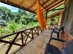 Whale Watching in Nuquí Private Eco Adventure (6 Days / 5 Nights) A wooden deck with chairs and orange hammocks overlooks a lush green jungle with banana plants and trees under a blue sky.