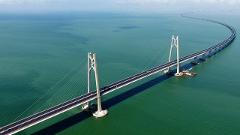 A long bridge curves across the sea, supported by tall towers and numerous pillars.