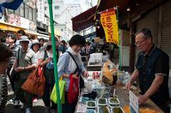 A bustling street scene in Japan showcases a vendor selling fresh seaweed-based delicacies to a diverse crowd of locals and tourists.