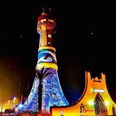 Full Day Tour To Siby And Bamako A vibrantly lit, unusually decorated tower stands tall against a dark night sky, with a smaller, brightly lit building to its right.