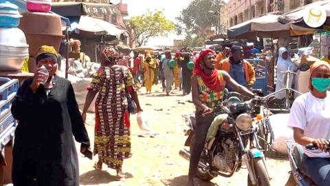 Full Day Tour To Siby And Bamako A diverse group of people are seen at a bustling market with motorcycles and goods on display.