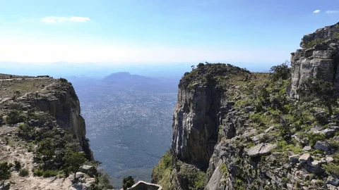 The image shows a breathtaking view of a valley from a high vantage point between two rocky cliffs, with a clear blue sky above.