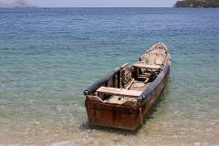 Cultural Caribbean Tour An old wooden boat sits on the shore of a tropical beach with calm, clear water and distant islands in the background.