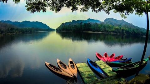 A serene view of boats docked on a lake surrounded by lush green mountains.