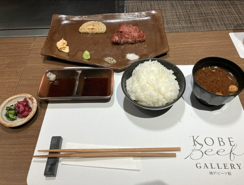 A set meal of Kobe beef with rice, miso soup, pickled vegetables, sauces, and condiments is displayed on a restaurant table.