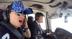 Two men are in a cockpit; one is focused on flying, while the other wears sunglasses and a hat, appears to be yelling.