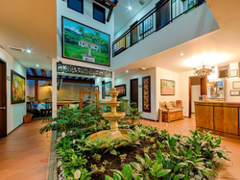 Birding - Cali, Coffee Region & Medellin This is a well-lit hotel lobby with a fountain, plants, artwork, reception desk, and a balcony on the second floor, showcasing a warm and inviting atmosphere.