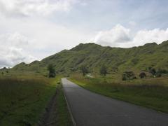 A winding asphalt road leads towards a green, hilly landscape under a cloudy sky in Papua New Guinea.