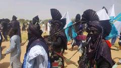 A group of men in Niger, West Africa, are dressed in elaborate black costumes and headdresses for the Bianou Festival, carrying spears and flags.