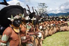 A line of tribesmen, adorned in traditional attire with painted faces and unique headdresses, play drums at the Mount Hagen Festival & Paiya Show.