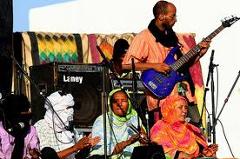 A band performs at the Agadez African Music Festival, featuring musicians playing instruments and singing, some wearing traditional head coverings.