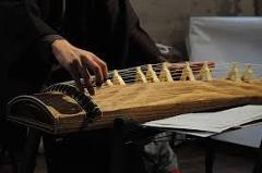 A person plays a Koto, a traditional Japanese stringed instrument, with sheet music nearby.