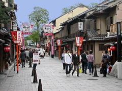 A bustling street scene in Japan with traditional architecture, lanterns, and people walking along a cobblestone path.