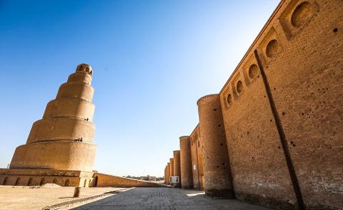 A low-angle shot showcases the Great Mosque of Samarra in Iraq, featuring its iconic spiral minaret against a clear blue sky.