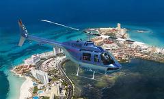 Caribbean Coast Helicopter Tour from Cancun A blue helicopter flies over a coastal city with beaches and turquoise water.