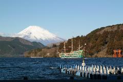 A vibrant green pirate ship cruises on a choppy lake with Mount Fuji in the background, and a traditional red gate on the shore.