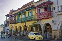In The Heart Of The Caribbean A colorful street scene in Cartagena, Colombia with colonial buildings featuring ornate balconies, arches, and a yellow taxi parked in the foreground.