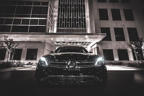 A black Mercedes-Benz GLE SUV is parked in front of a modern building with illuminated windows and a sleek awning.
