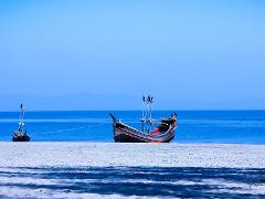 Two wooden boats sit on a white sand beach under a clear blue sky, connected by a taut rope and contrasting against the tranquil blue sea.