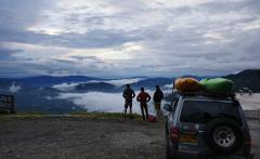 Kayak Adventure - 10 Days Three people stand on a hilltop overlooking a valley filled with low-lying clouds, with a car carrying kayaks parked nearby.