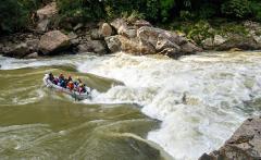 White Water Rafting the Samana River A group of people in a raft navigate through the rough rapids of a river surrounded by rocks and lush greenery.