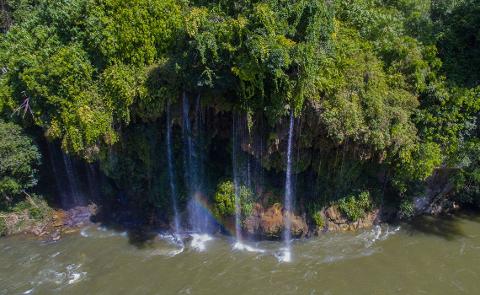 White Water Rafting the Samana River An aerial view of a cascading waterfall with lush greenery and a vibrant rainbow arching through the falling water.