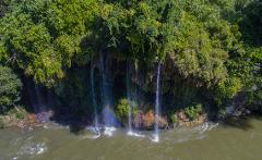 White Water Rafting the Samana River An aerial view of a cascading waterfall with lush greenery and a vibrant rainbow arching through the falling water.