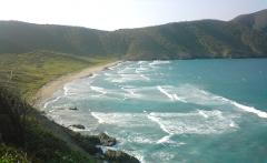 Cultural Caribbean Tour A scenic view of a bay with waves crashing on a sandy beach, surrounded by lush green hills.